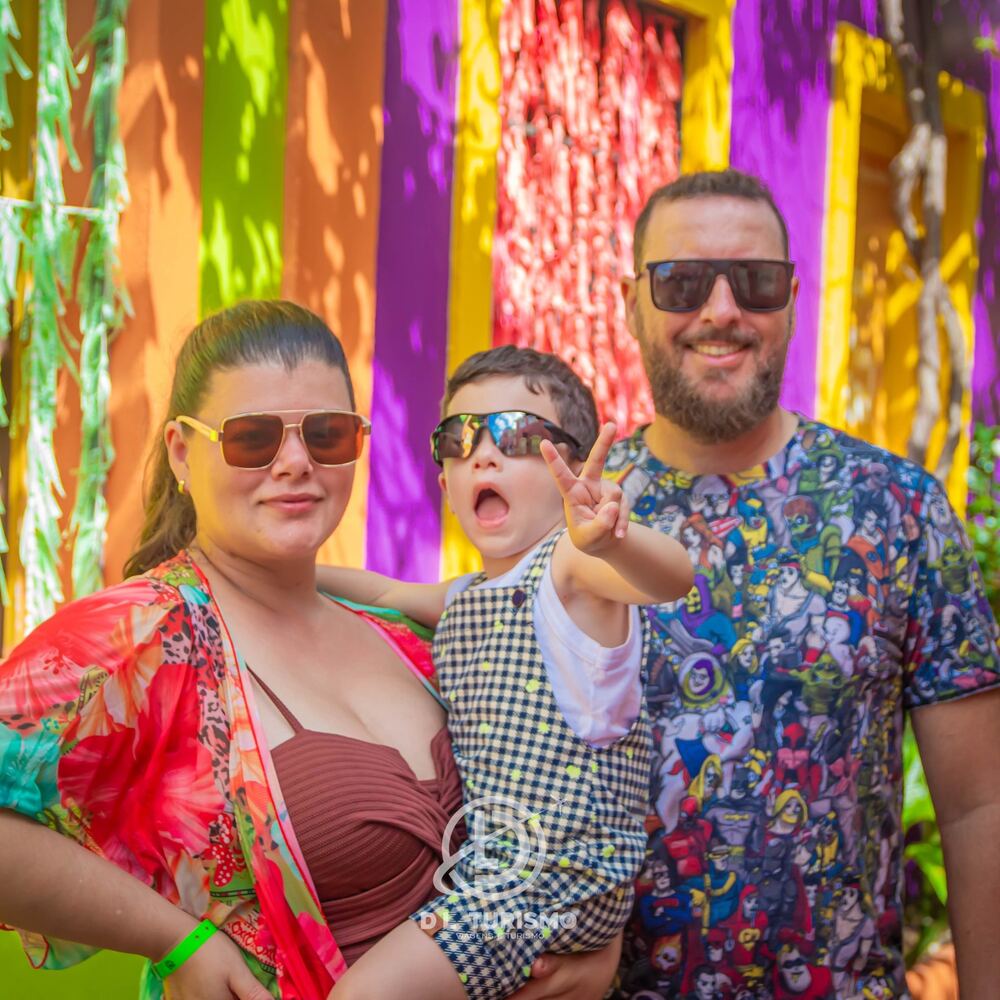 Família de óculos escuros sorrindo diante de uma parede colorida
