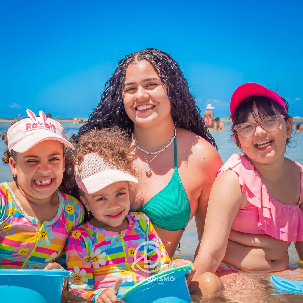 Crianças e uma jovem sorrindo na água rasa